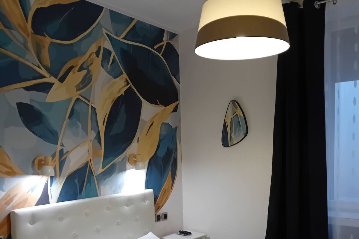 Un lit bien fait, avec du linge de lit blanc, une tête de lit capitonnée et une table de chevet avec une lampe.
