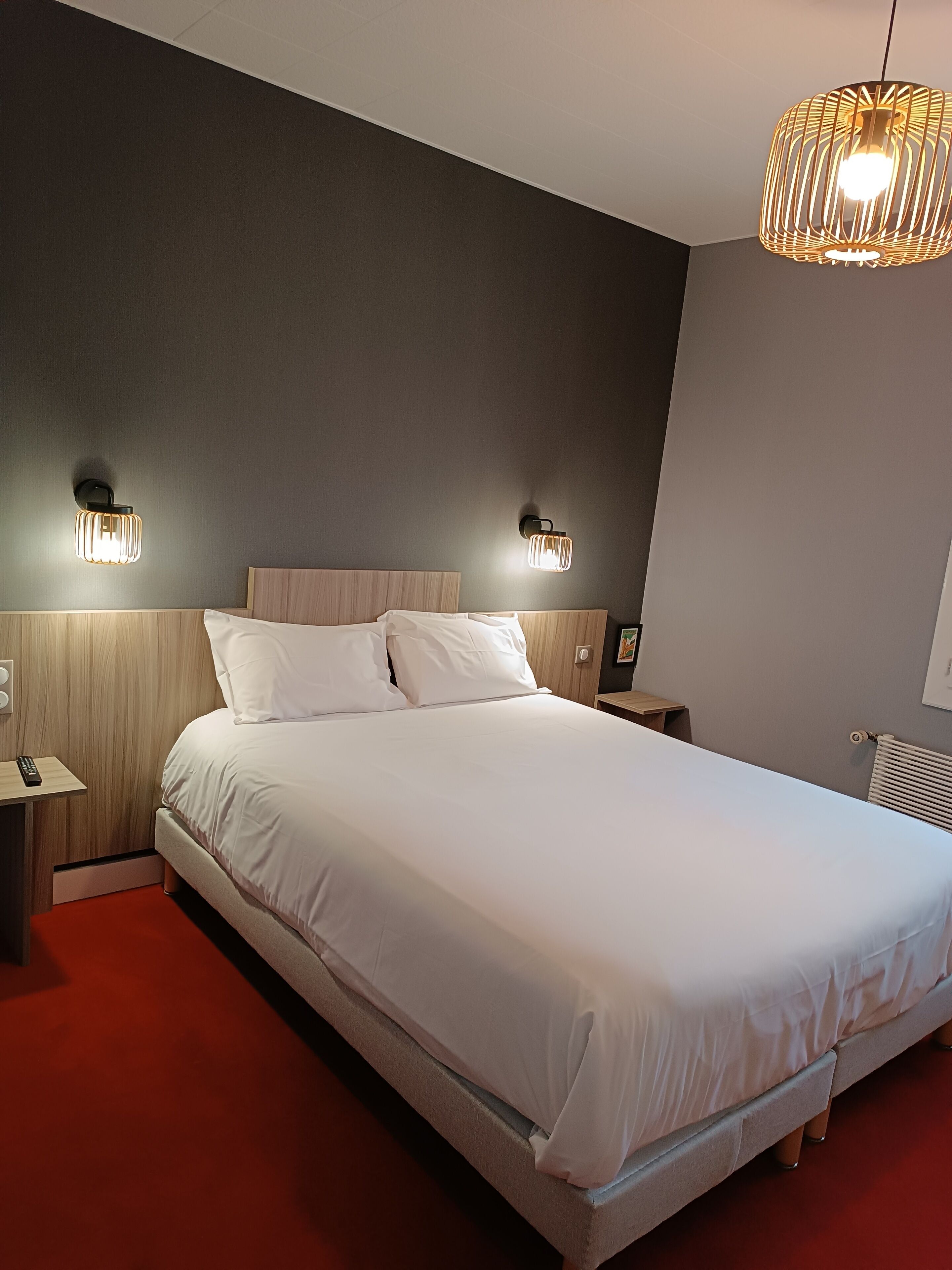 Ein modernes Hotelzimmer mit einem großen Bett, zwei Nachttischen, einer Stehlampe und einer Deckenleuchte.