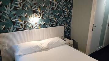 A hotel room with a bed, a nightstand, a wall-mounted lamp, and a door.
