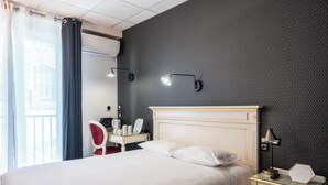 Een hotelkamer met een bed, nachtkastje, lamp en een bureau met stoel.