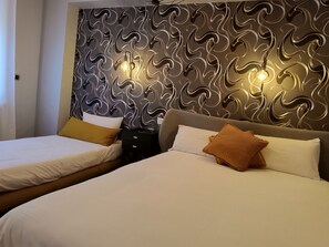 Two beds with white linens and a variety of pillows, including a decorative headboard with integrated lighting.