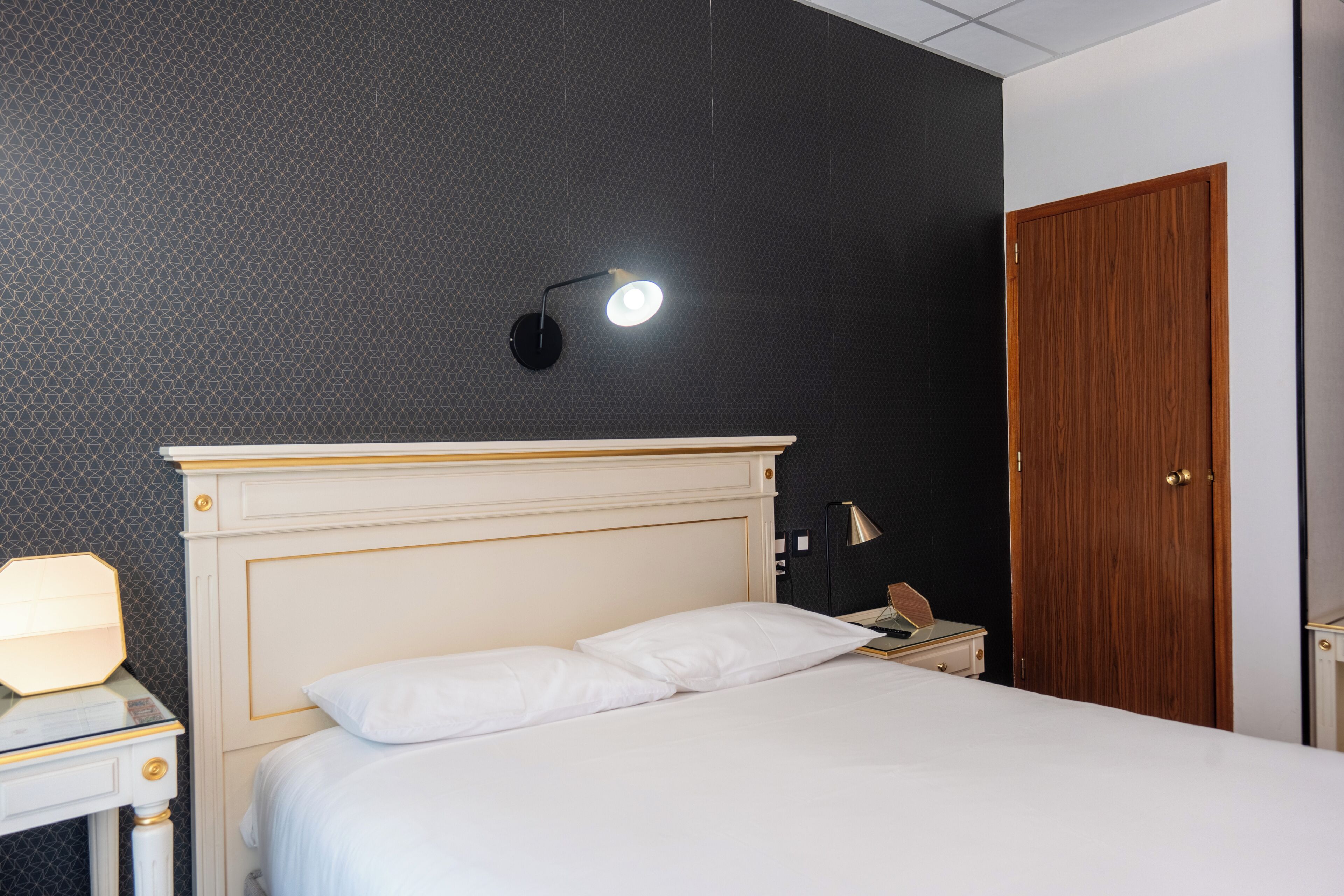 Un lit bien fait, avec du linge de lit blanc, une lampe de chevet et une porte en bois.