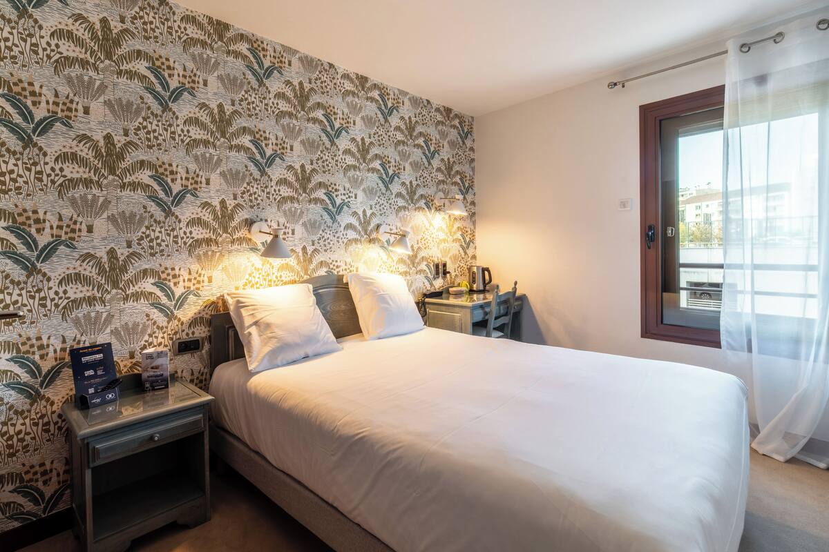 Une chambre d’hôtel avec un lit, des tables de chevet, un bureau et une fenêtre avec des rideaux.