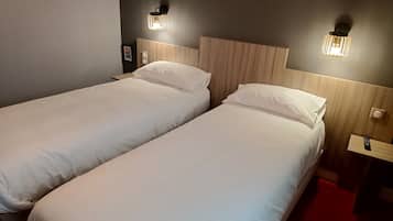 A hotel room with two single beds, a wooden headboard, bedside tables with lamps, and a red carpet.