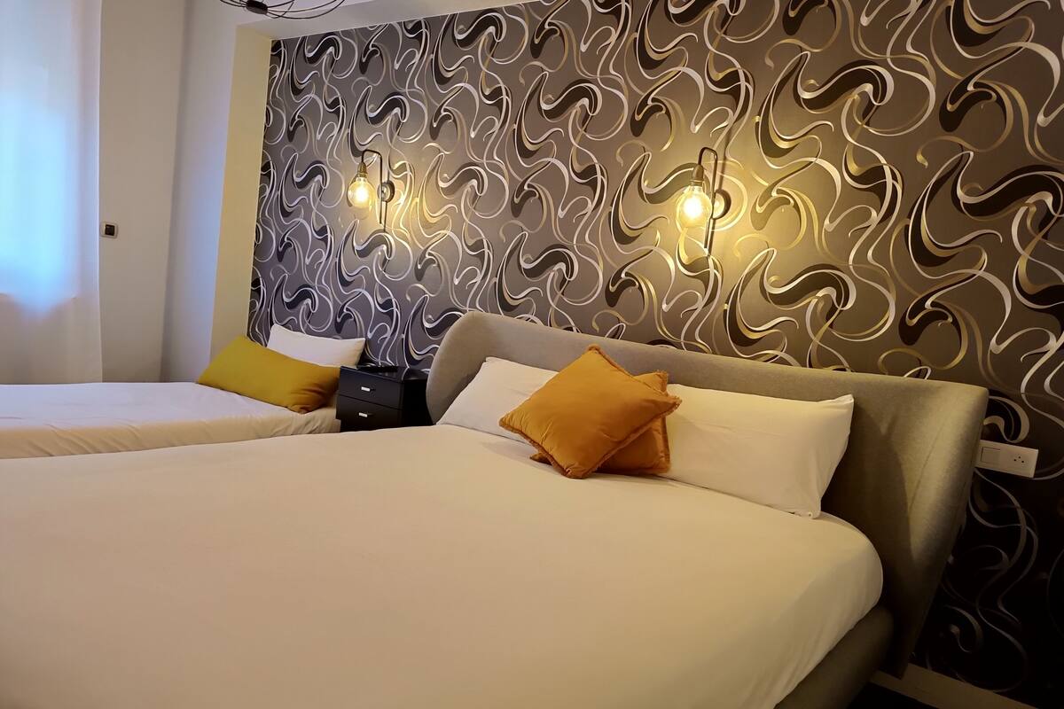 Une chambre d’hôtel avec deux lits, un papier peint à motifs et une table de chevet avec une lampe.