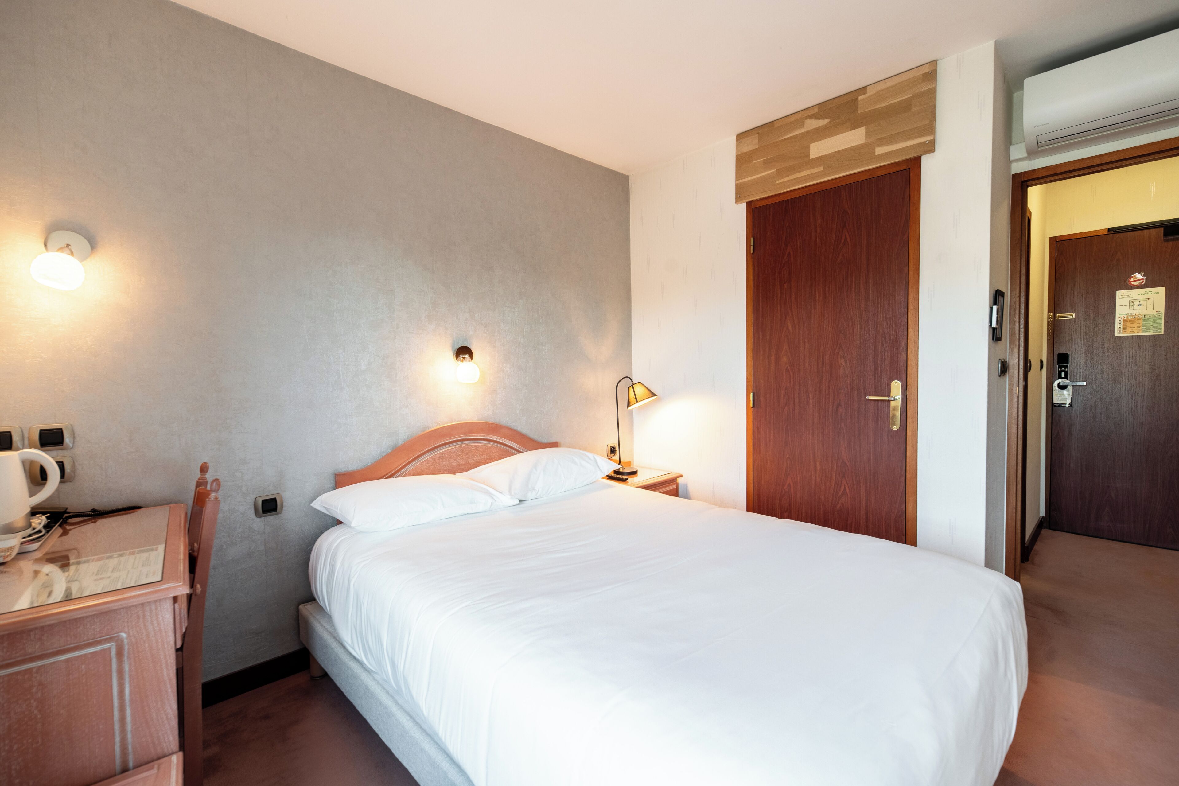 A hotel room with a bed, bedside table, lamp, and a wooden wardrobe.