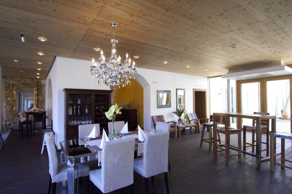 A dining area with a chandelier, wooden ceiling, and a bar area with shelves and glasses.