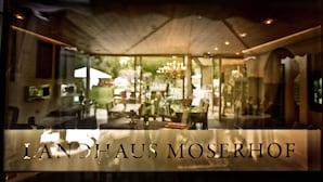 A modern interior with a glass wall, a chandelier, and a sign reading "LANDHAUS MOSERHOF". - Hotel Landhaus Moserhof (Gumpoldskirchen)