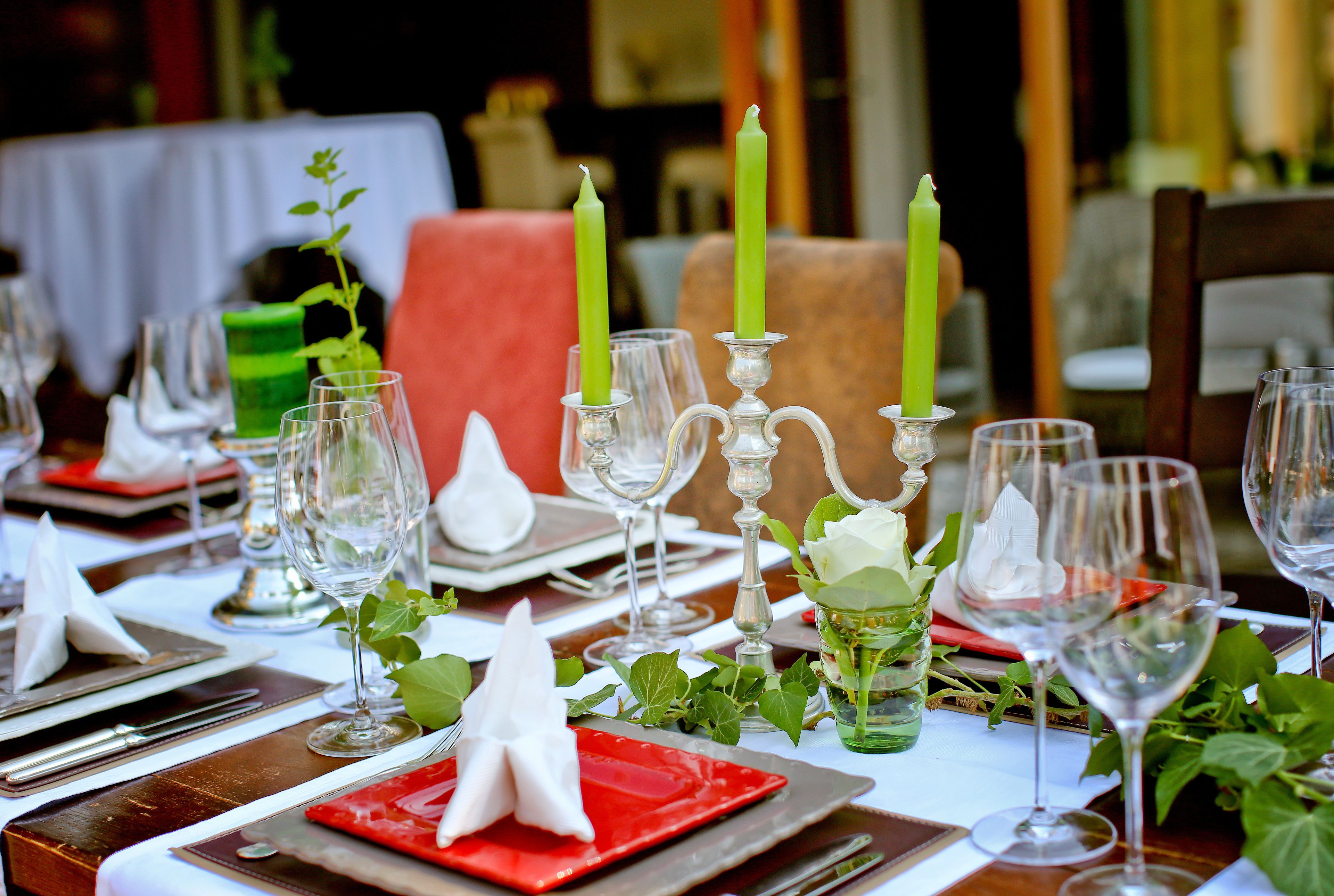 Une table dressée pour un dîner formel, avec de la vaisselle transparente, des serviettes rouges et des bougies vertes.