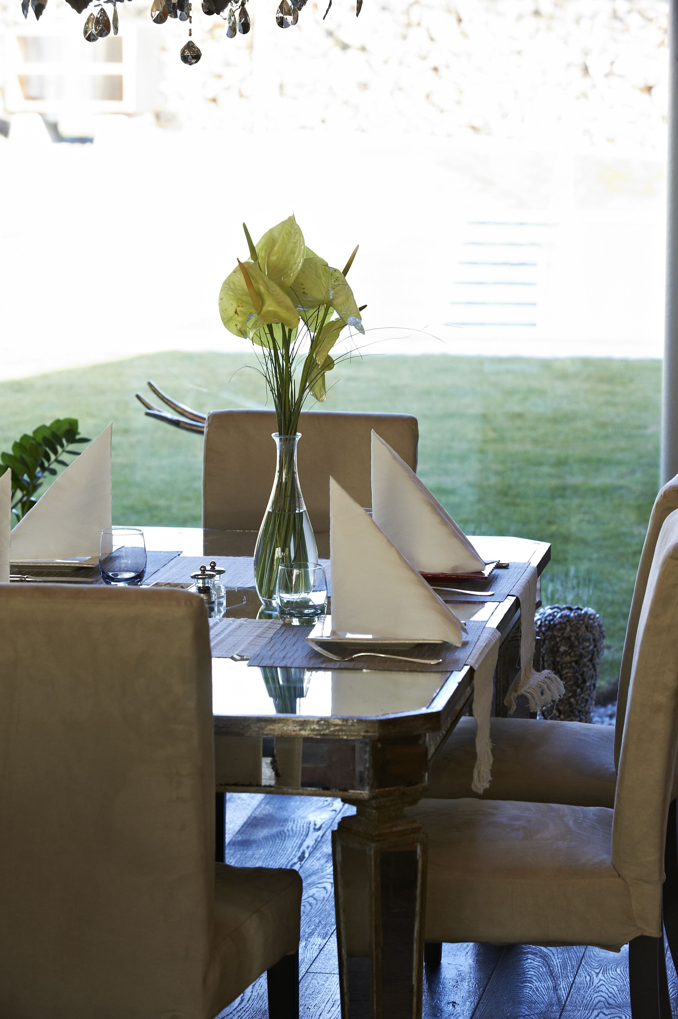 A dining table set for four with a vase of yellow flowers, clear glasses, and neatly folded napkins.