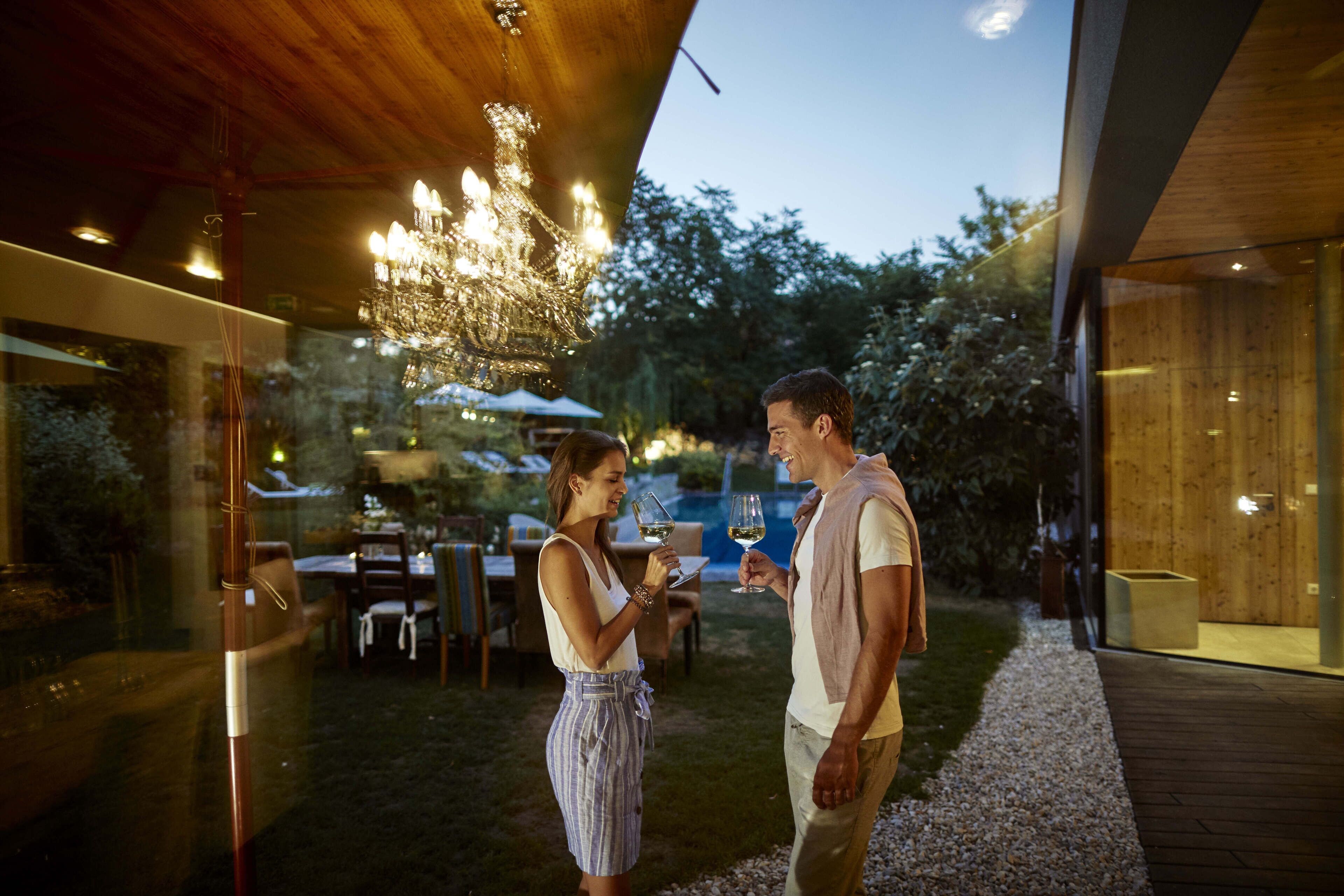Un área de comedor al aire libre con mesas y sillas, una pérgola de madera y un cerramiento de vidrio.
