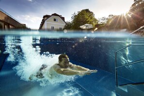 A swimming pool with a person swimming, a clear sky, and a house in the background.