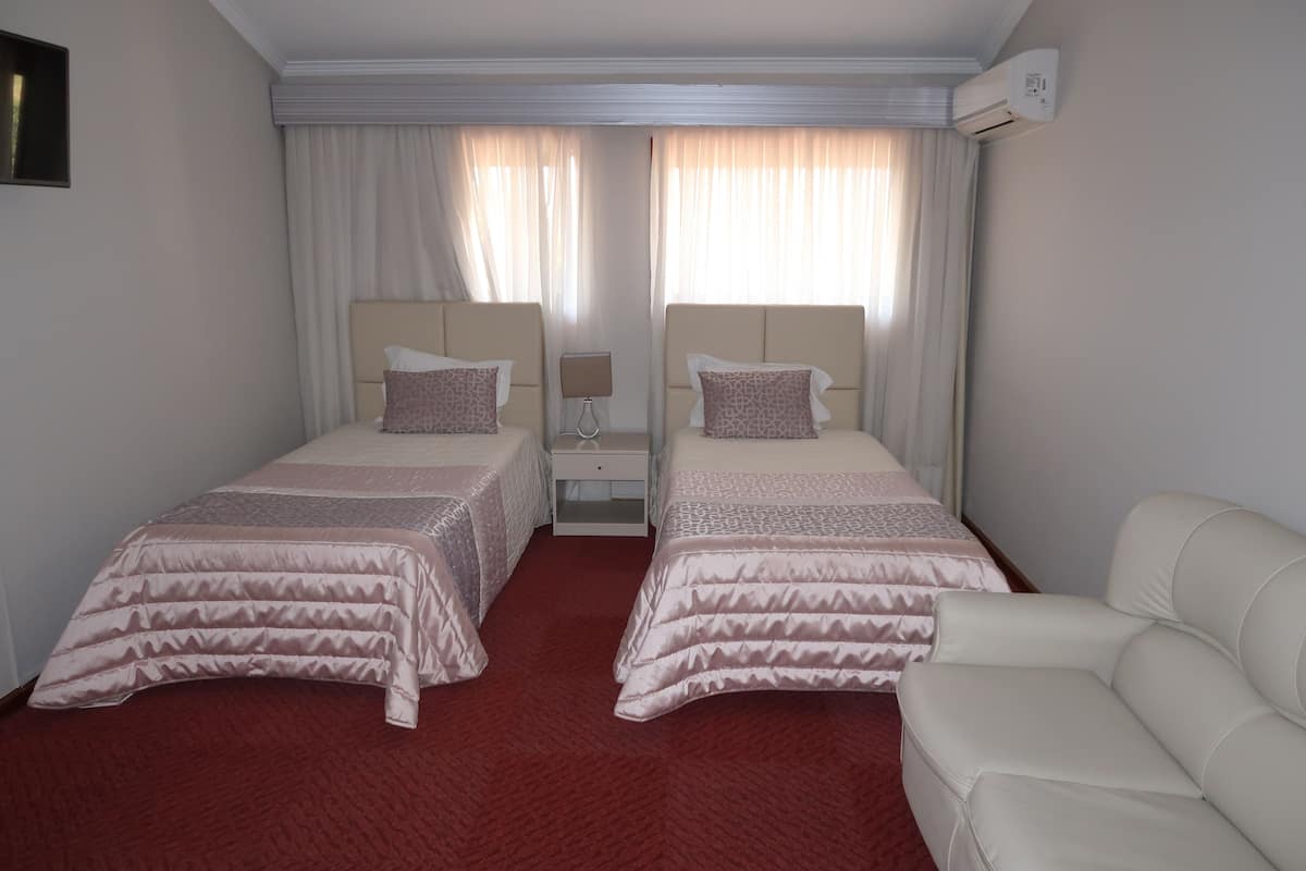 A hotel room with two beds, a red carpet, a white sofa, and an air conditioning unit.