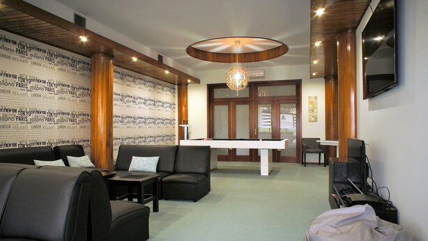 Un hall con mesa de billar, asientos de cuero y una pared con nombres de ciudades.