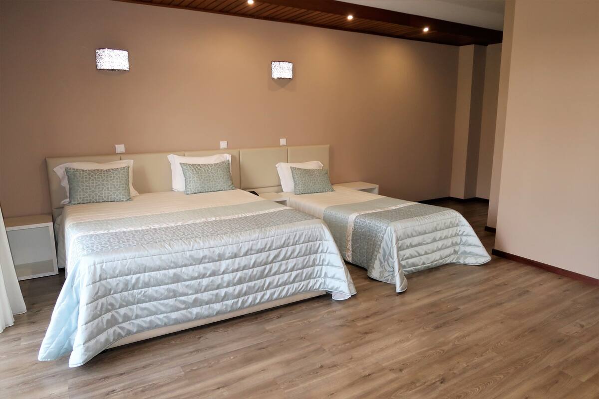 A hotel room with two beds, each with a patterned bedspread and matching pillows. There are bedside tables with lamps and a wooden ceiling with recessed lighting.