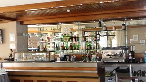 Zona de bar con estantes llenos de botellas, una máquina de café y una vitrina de cristal.