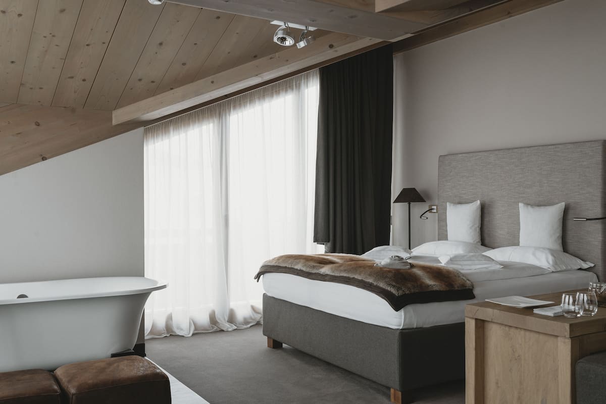 A modern bedroom with a large bed, a wooden ceiling, a bathtub, and a bedside table.