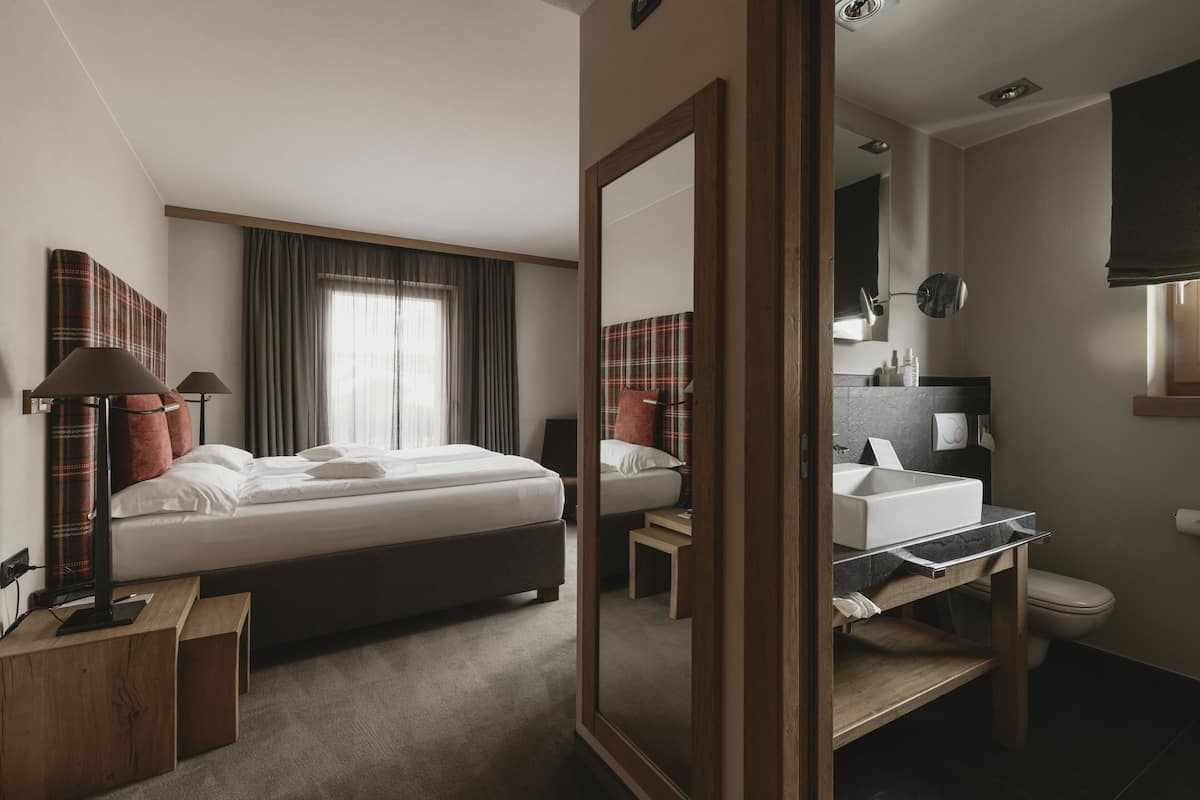 A hotel room with a bed, bedside tables, a mirror, a bathroom with a sink and toilet.