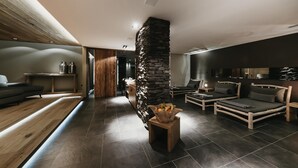 A modern living room with a stone pillar, dark flooring, and a wooden bench. - Eco & Wellness Boutique Hotel Sonne (Livigno)