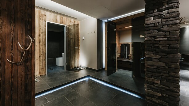 A modern interior with a stone accent wall, a wooden door, and a tiled floor. - Eco & Wellness Boutique Hotel Sonne (Livigno)