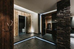 A modern interior with a stone accent wall, a wooden door, and a tiled floor. - Eco & Wellness Boutique Hotel Sonne (Livigno)