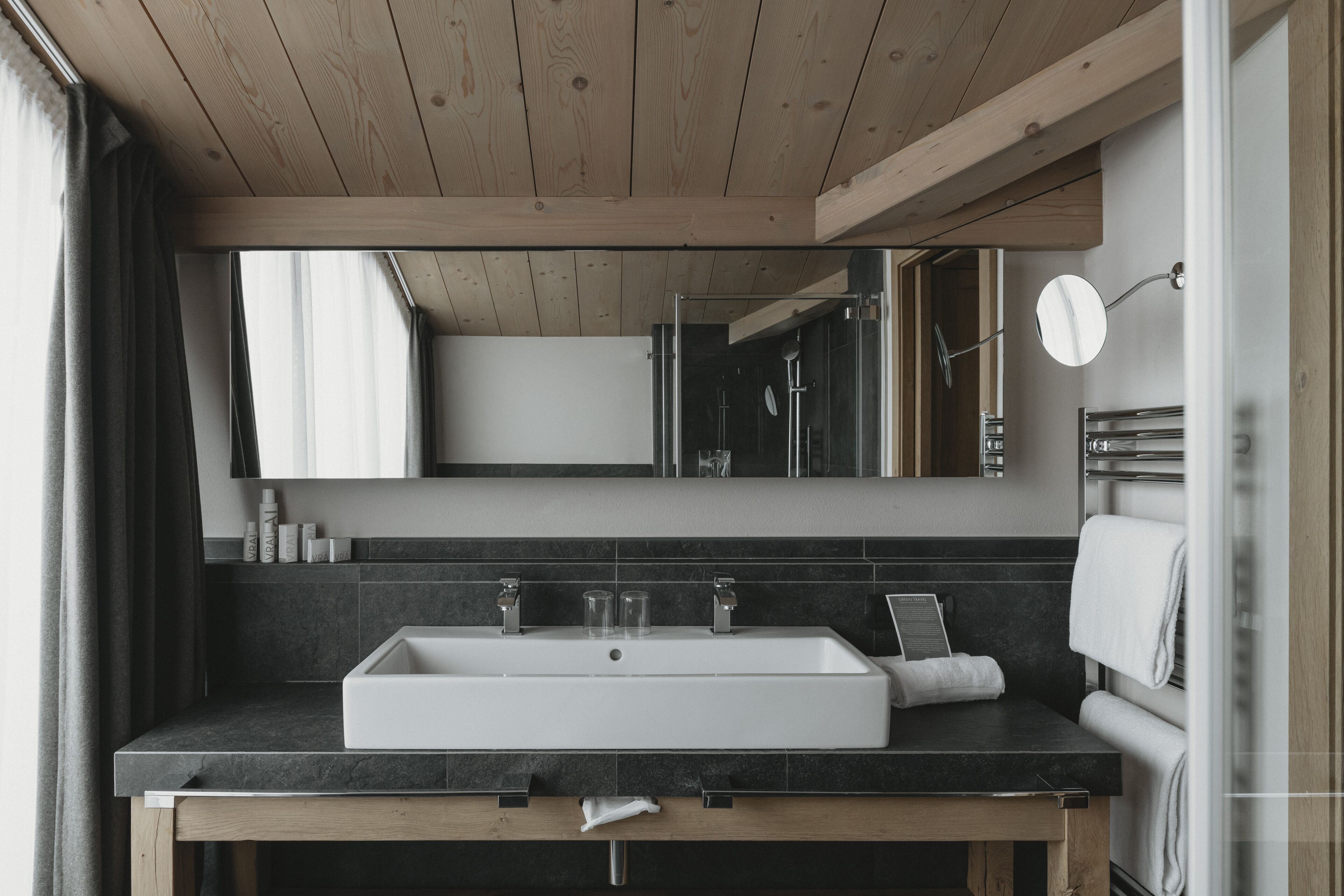 Un baño moderno con un lavamanos grande blanco, encimeras oscuras y techo de madera.