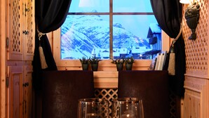 A cozy seating area with a view of snow-covered mountains through a window, featuring a wicker table with candles and a lamp. - Eco & Wellness Boutique Hotel Sonne (Livigno)