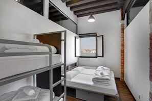Habitación de hotel compacta con literas, una ventana con vista a la ciudad y una pared de ladrillo.
