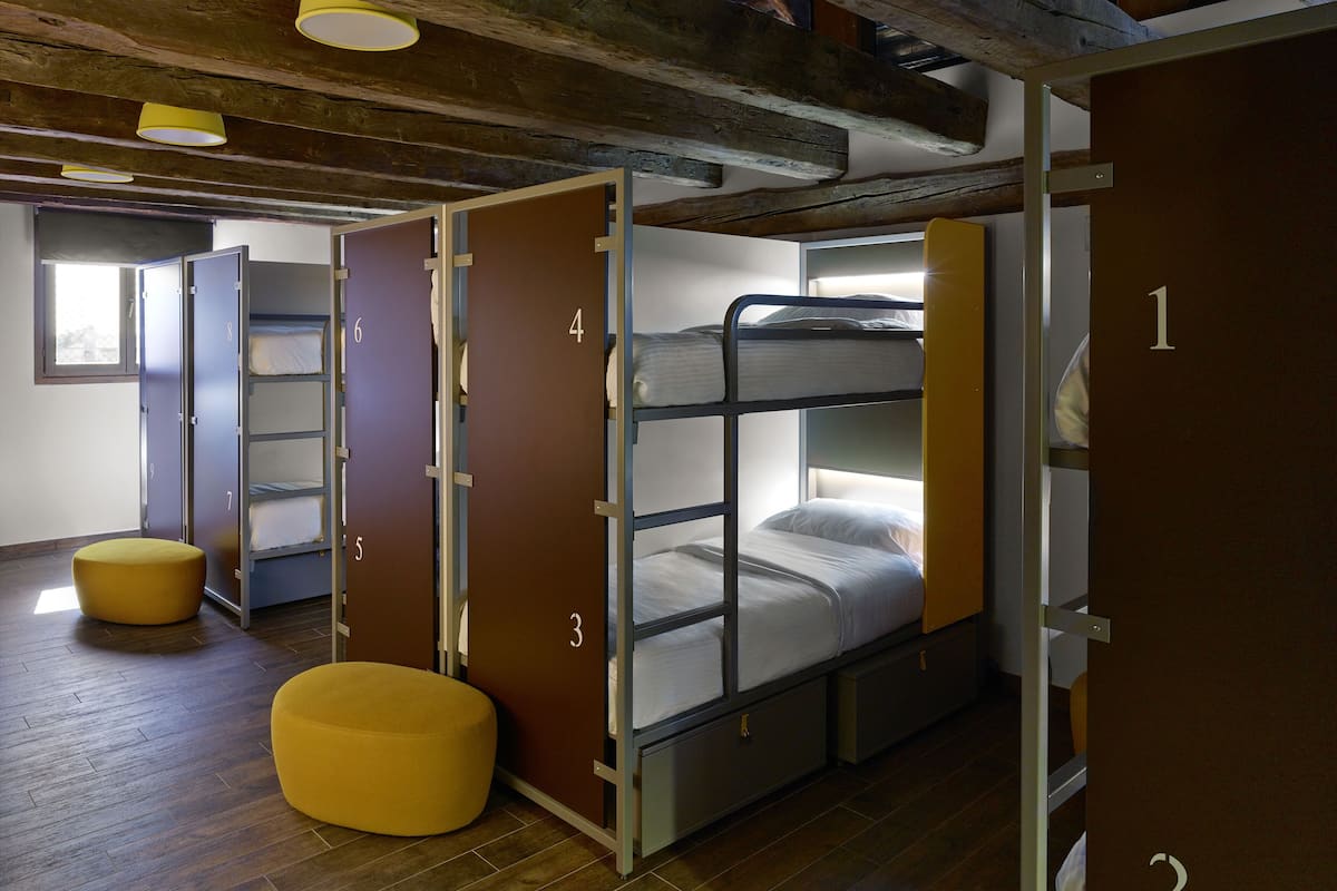 A dormitory room with bunk beds, a yellow ottoman, and a wardrobe with numbered doors.