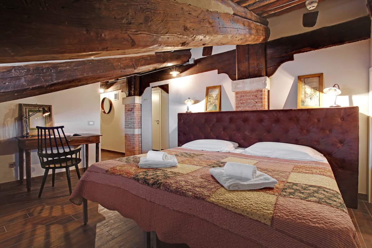 A bedroom with a large bed, a wooden desk, a chair, and a fireplace.