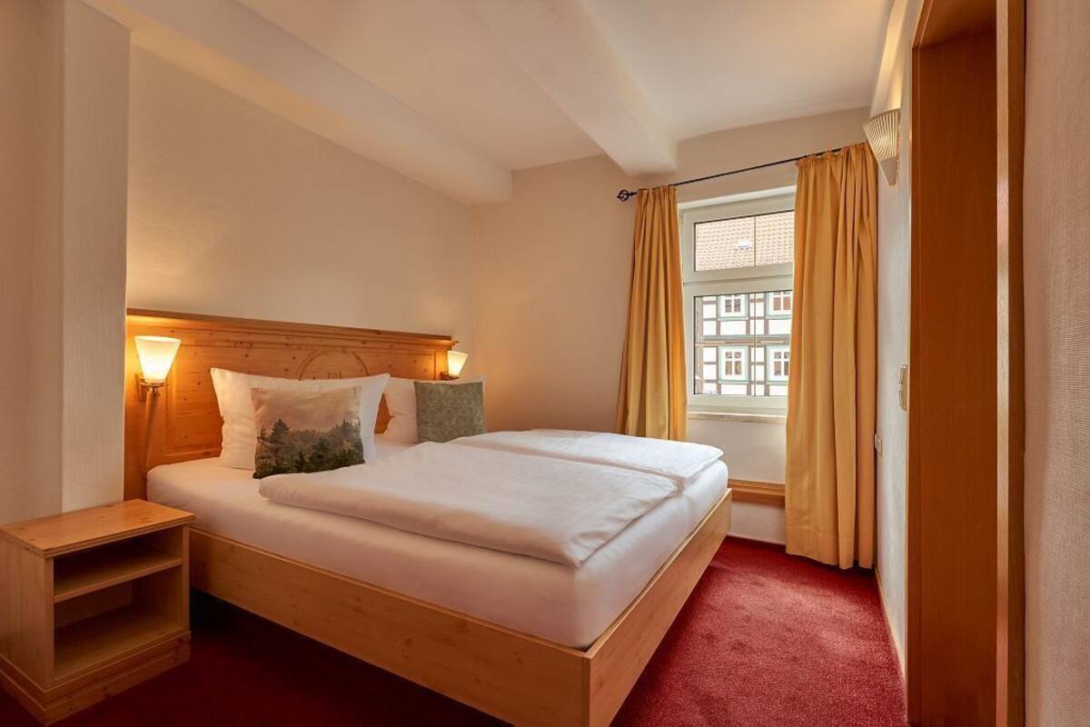 Una cama doble con cabecera de madera, dos mesitas de noche y una ventana con cortinas.