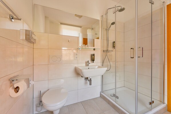Un baño moderno con inodoro, lavamanos y ducha con mampara de vidrio.