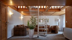 A cozy living room with a spiral staircase, wooden walls, and a large potted plant. - Hotel Schlossblick (Wernigerode)