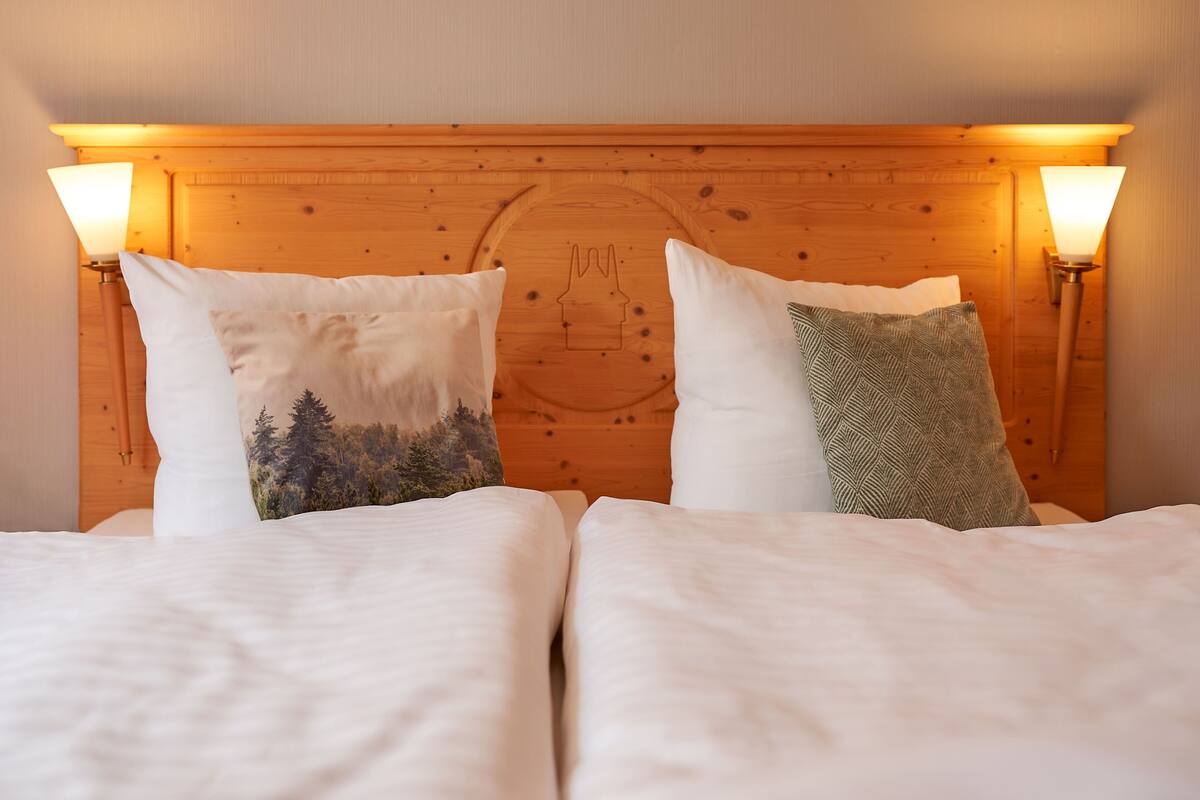 Una cama doble con dos almohadas, una con diseño de bosque y otra con un motivo geométrico.