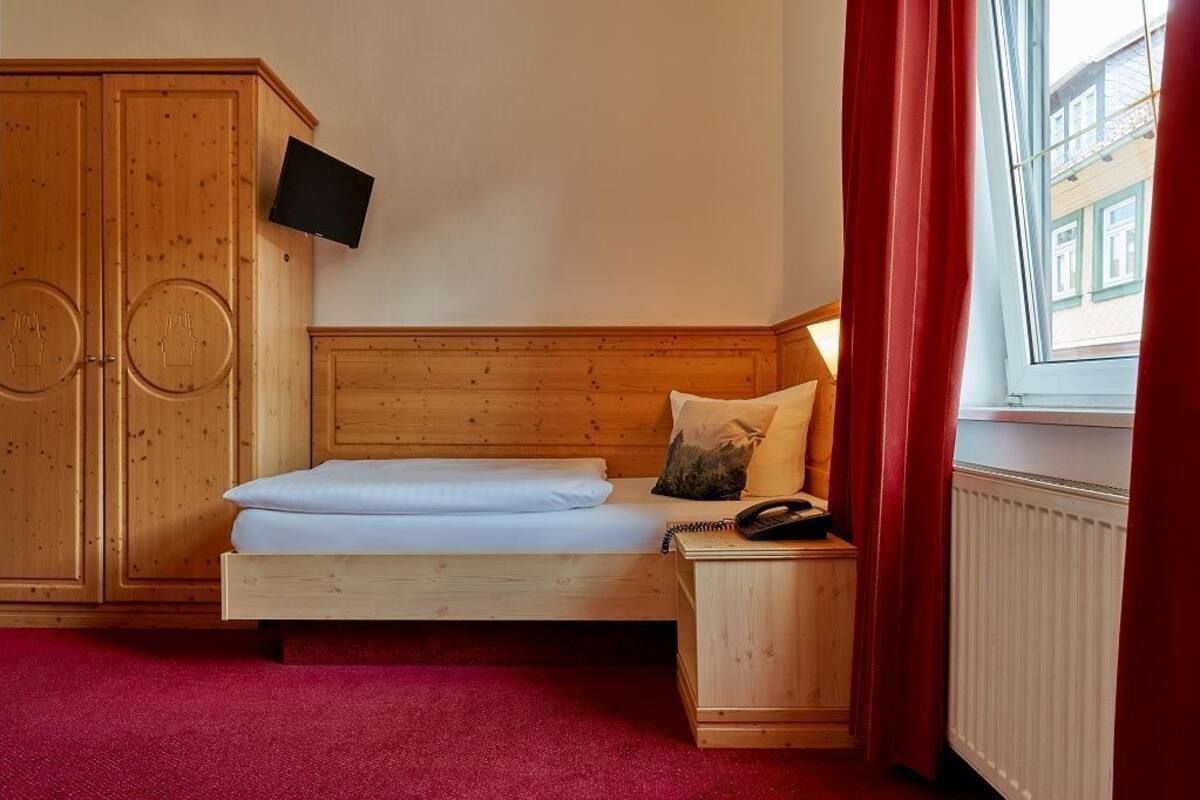 Un dormitorio con una cama de madera, una mesita de noche, un televisor montado en la pared y una ventana con cortinas rojas.