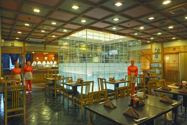 A restaurant with a central glass enclosure, wooden tables and chairs, and staff in uniforms.