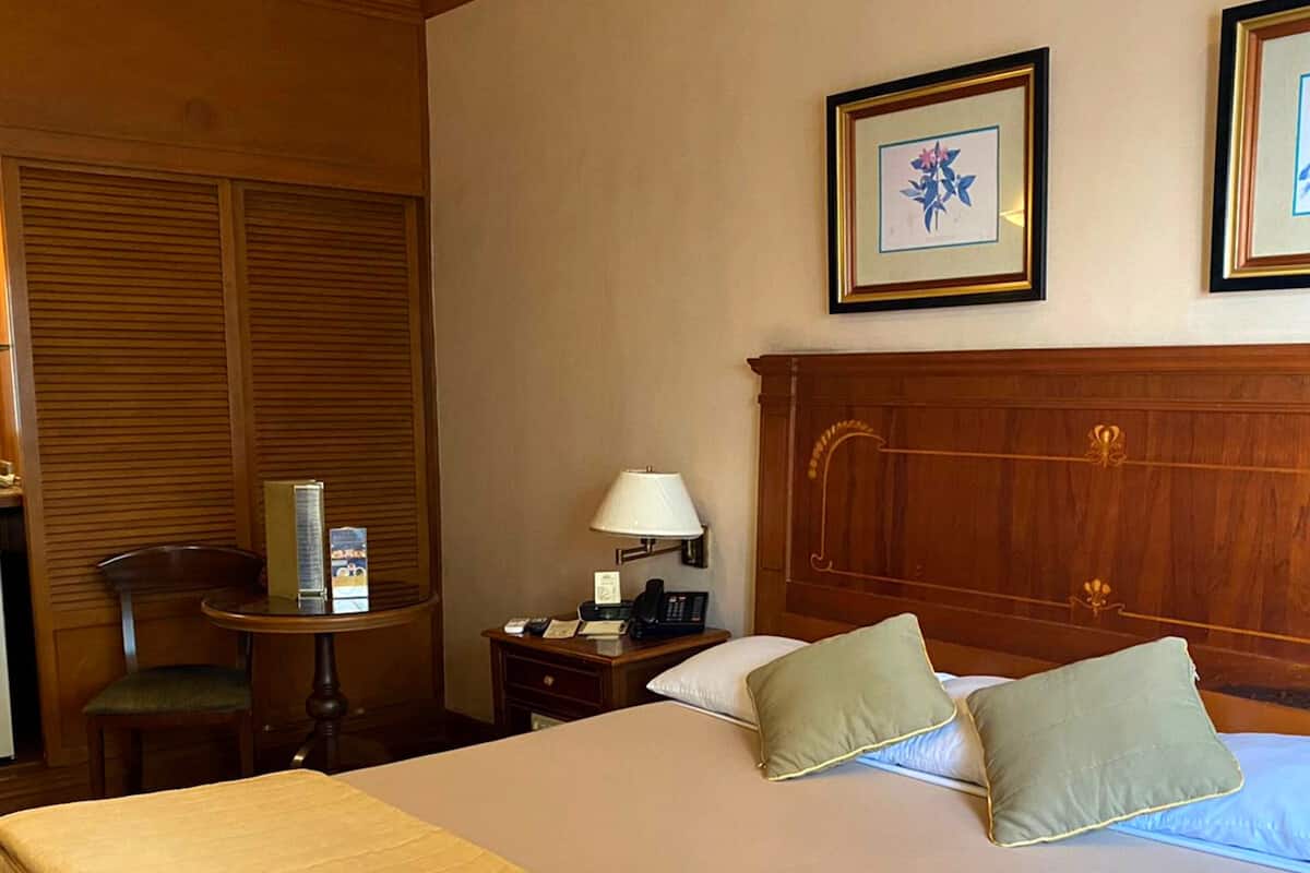 Une chambre d’hôtel avec un grand lit, une tête de lit en bois, une table de chevet avec une lampe, une chaise et un bureau avec un téléphone.