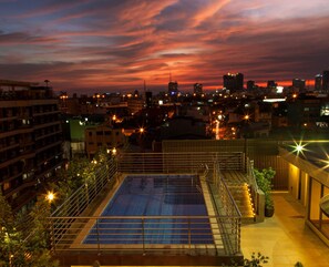 A rooftop pool with a cityscape view at dusk.