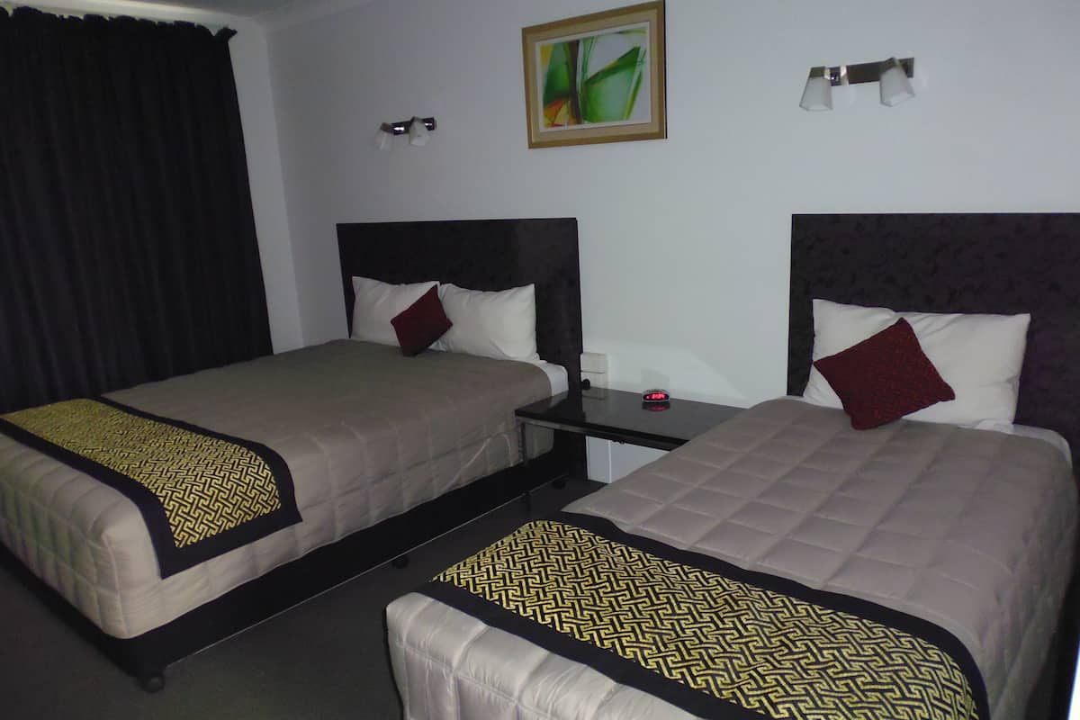 A hotel room with two beds, each with a headboard, a bedside table, and a nightstand.