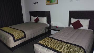 Una habitación de hotel con dos camas, cada una con cabecera, mesita de noche y mesilla.