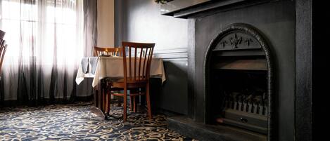 A dining area with a table set for two, a fireplace, and a patterned carpet.