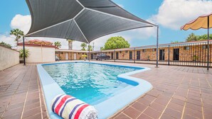 A swimming pool with a shaded area, tiled deck, and a striped towel. - Burke and Wills Motor Inn (Kingaroy)