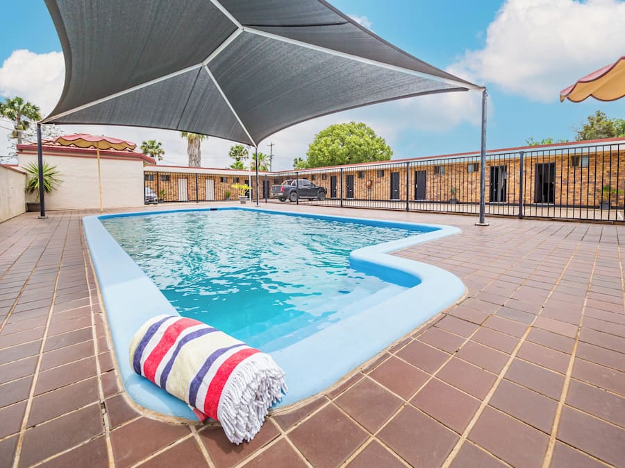 A swimming pool with a shaded area, tiled deck, and a striped towel.