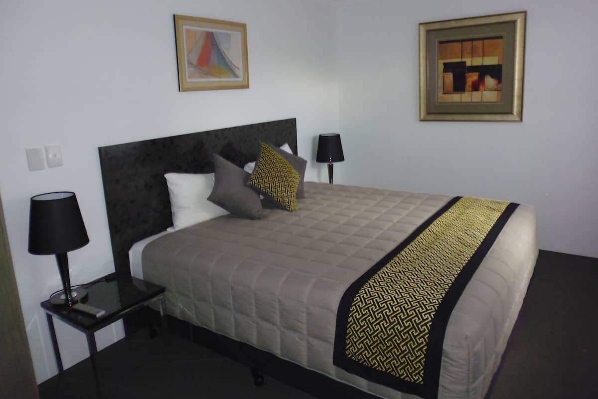 A neatly made bed with a quilted headboard, a bedside table with a lamp, and two framed artworks on the wall.