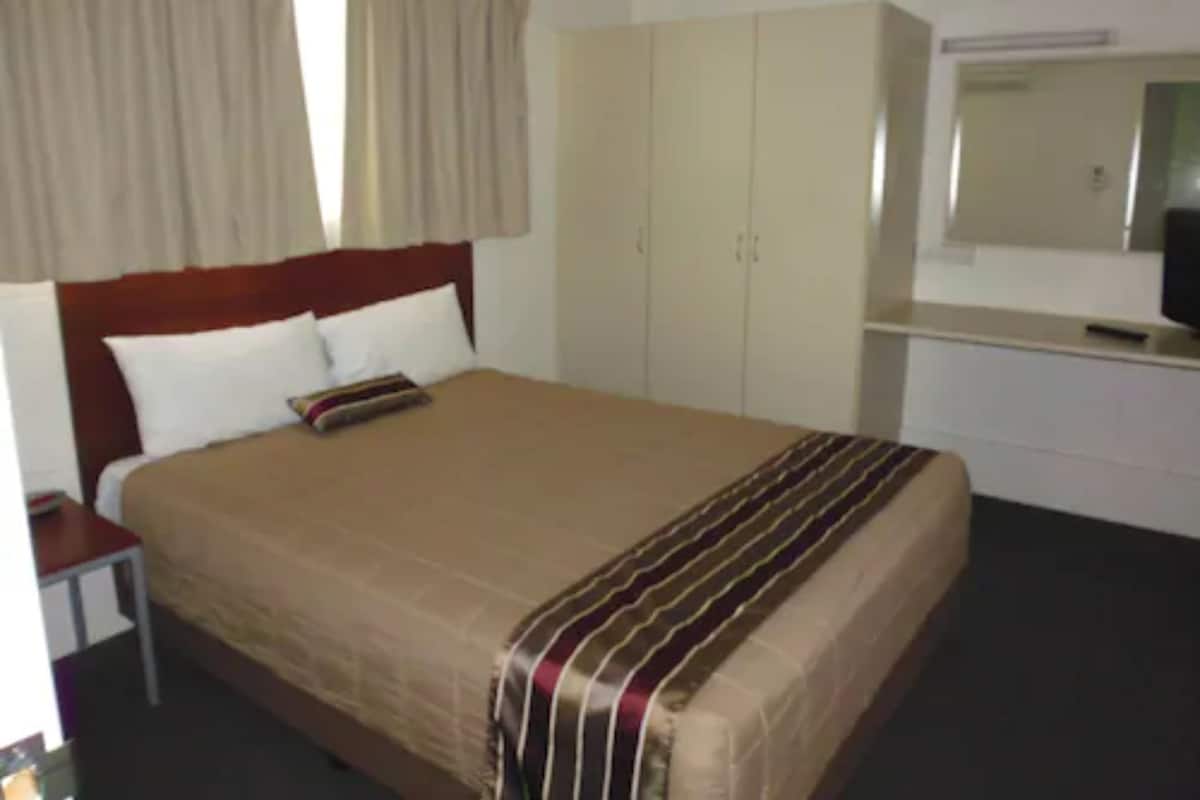 A hotel room with a large bed, a bedside table, a wardrobe, and a mirror.