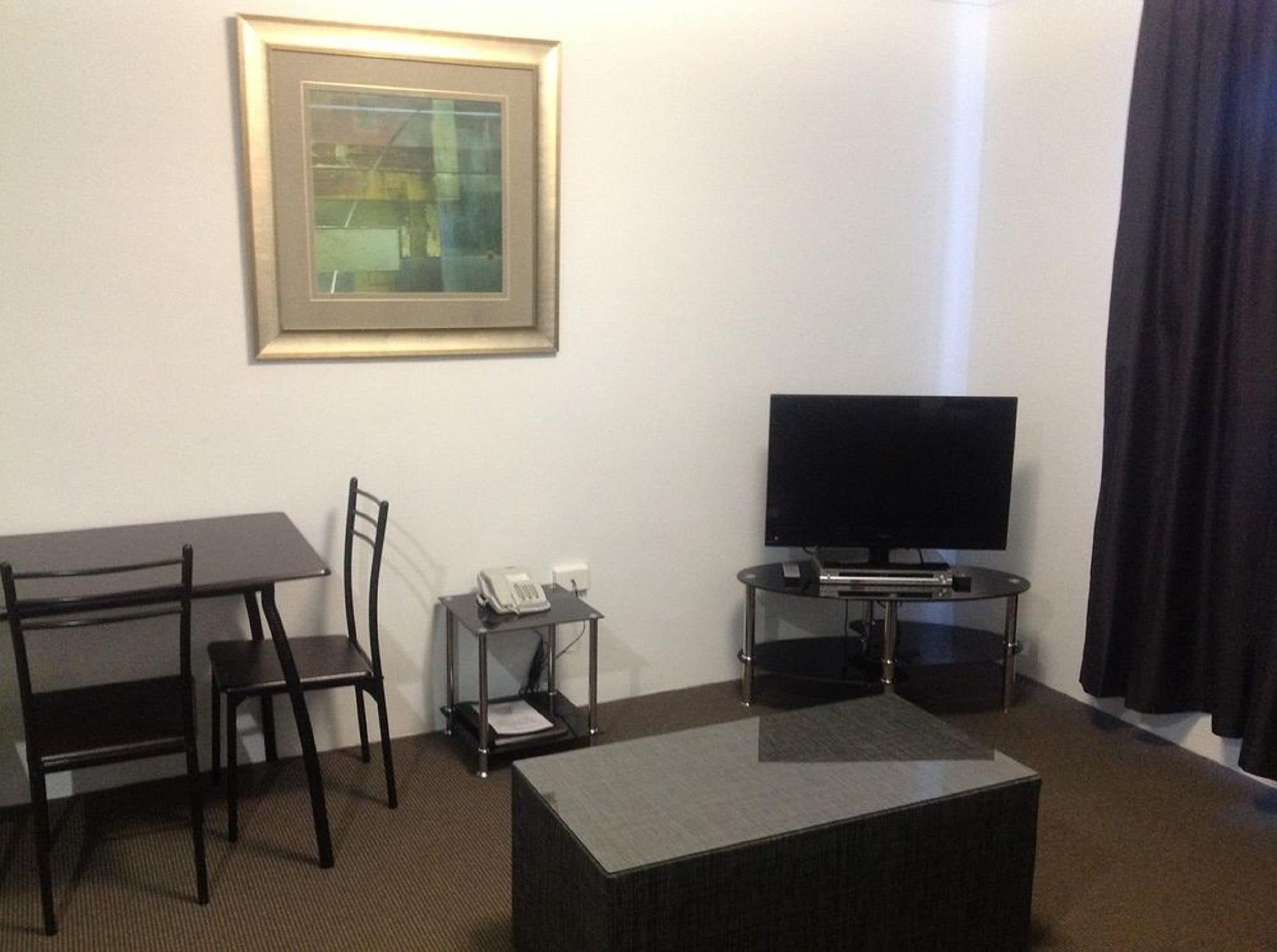 Ein Hotelzimmer mit Fernseher, Schreibtisch, Stuhl, Telefon und einem gerahmten Bild an der Wand.