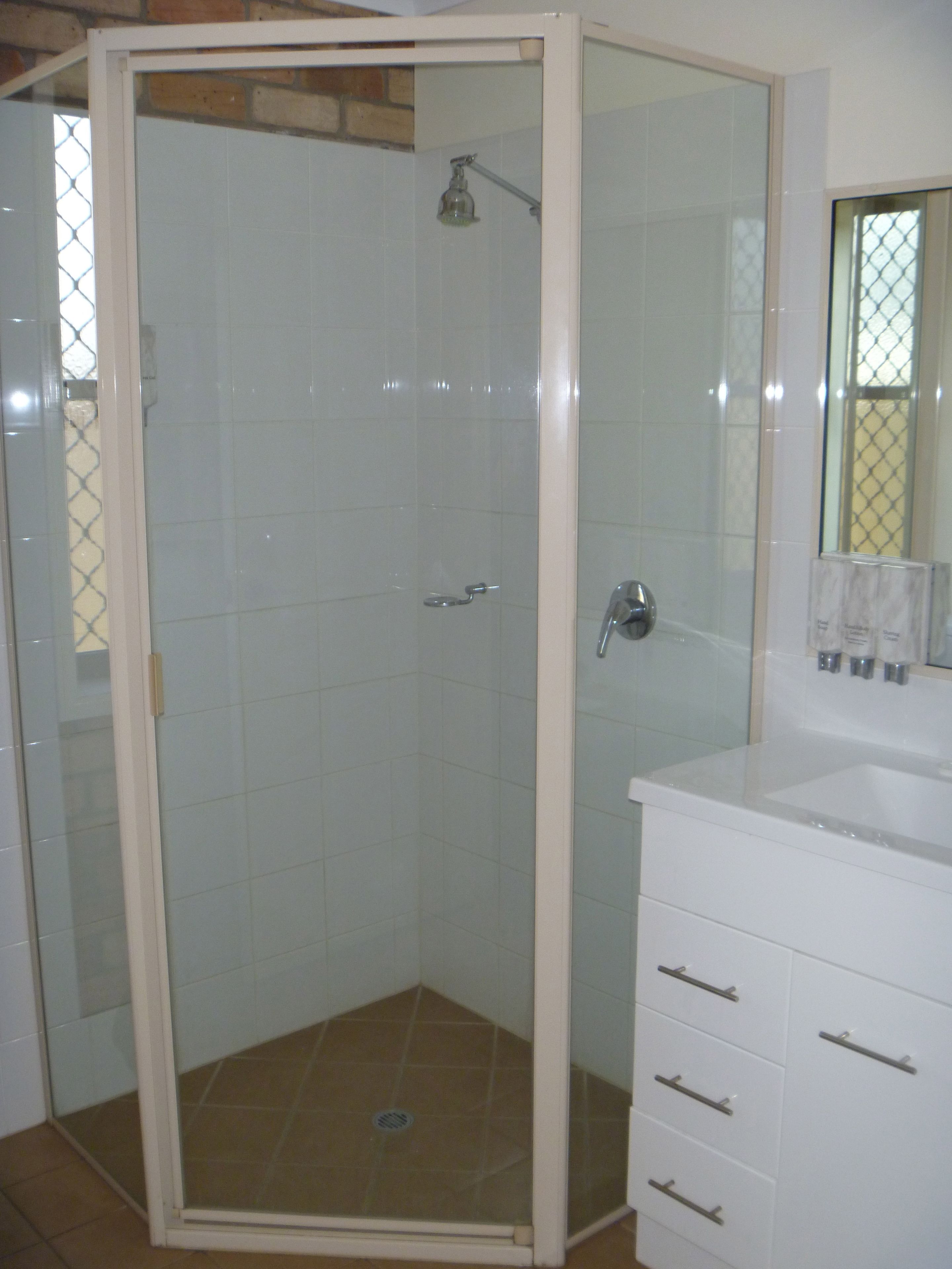 A bathroom with a glass-enclosed shower, white cabinets, and a mirror.