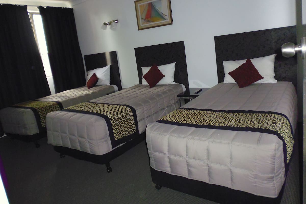 A hotel room with two single beds, each with a patterned bedspread and pillows.