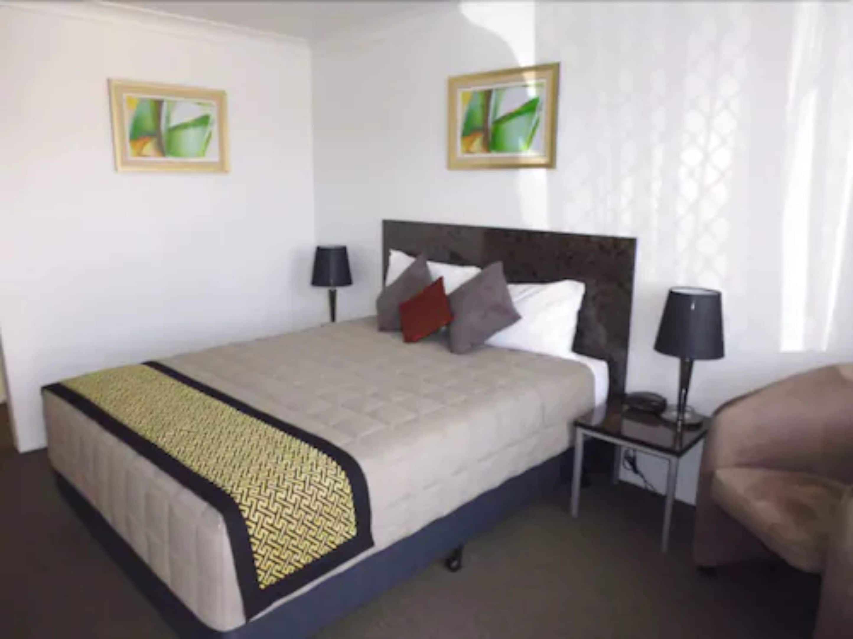 A hotel room with a bed, two bedside tables, a chair, and two abstract paintings on the walls.