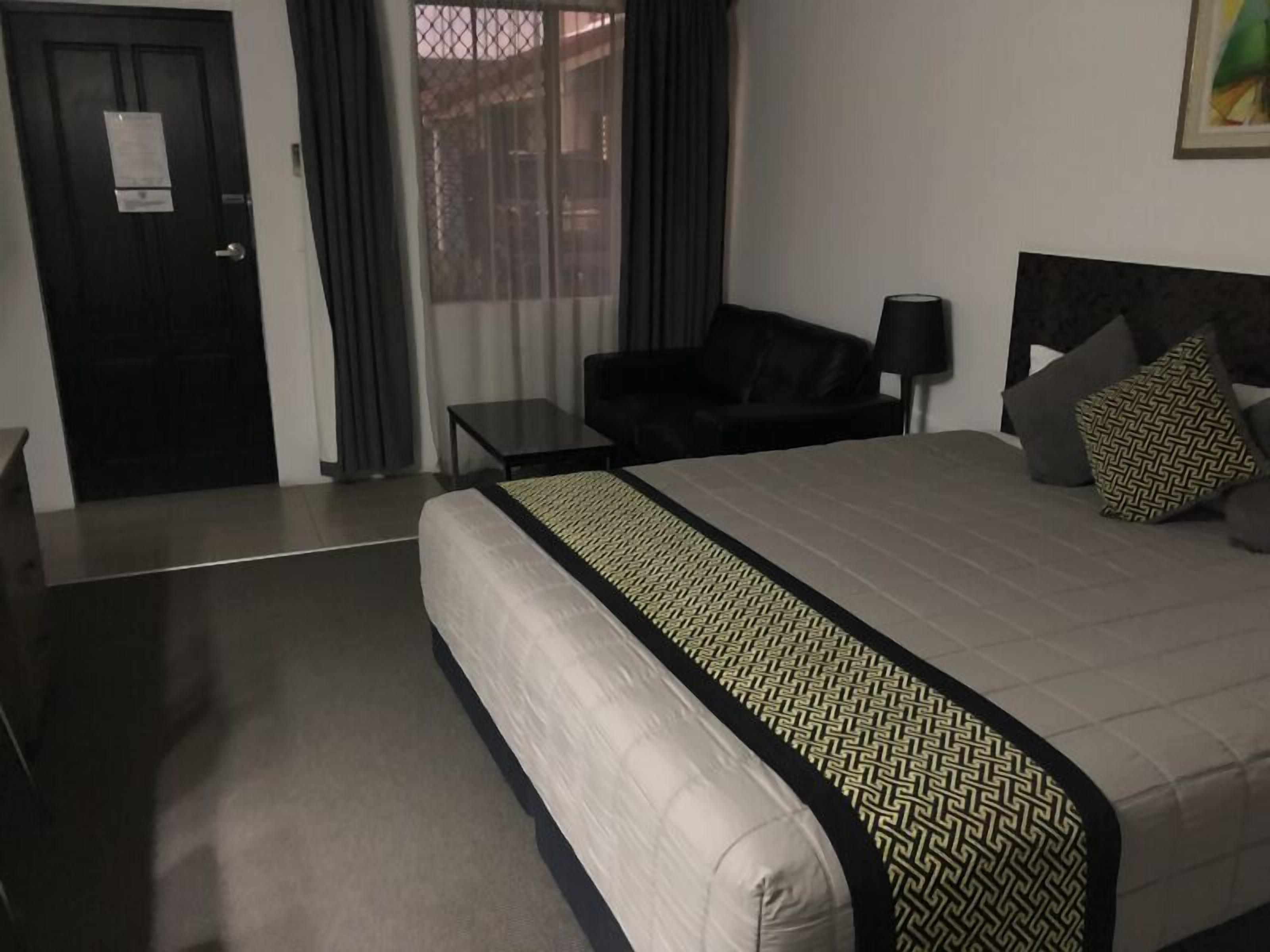 A hotel room with a large bed, a small table, a sofa, and a door.